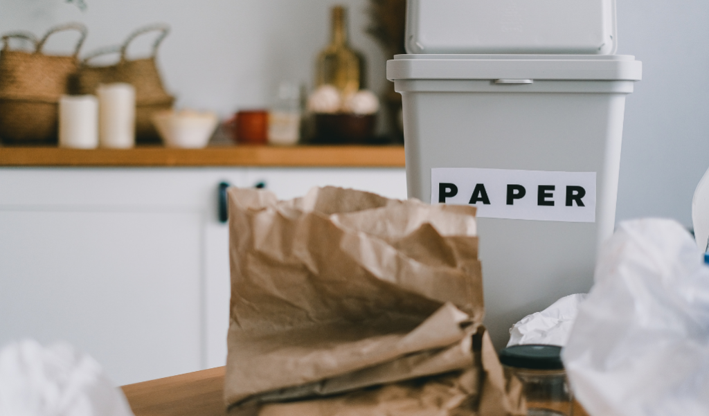 Recyclable paper next to a recycling bin in a kitchen.