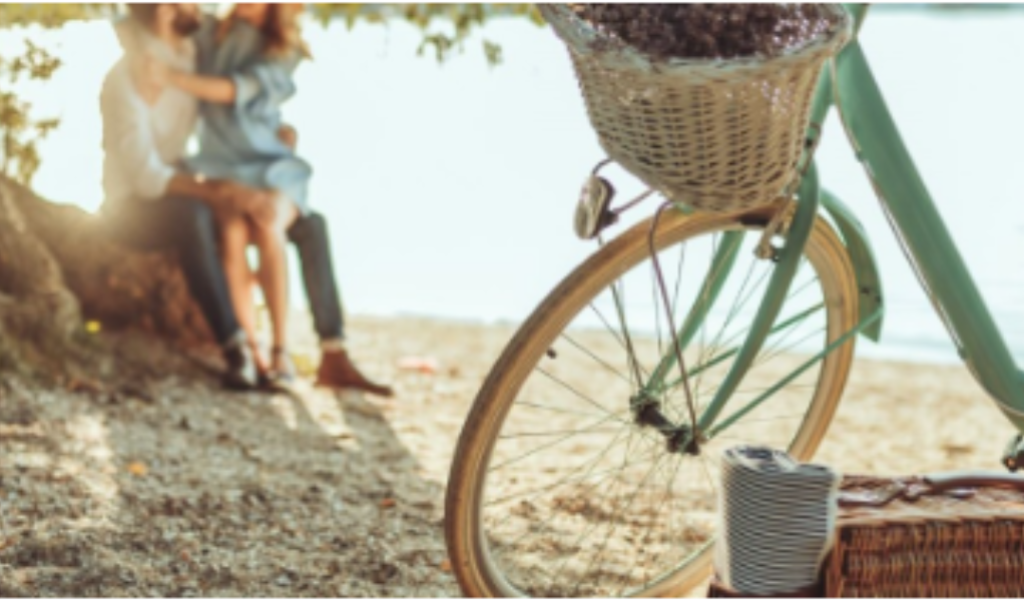 Couple by the beach with a bike and picnic basket.