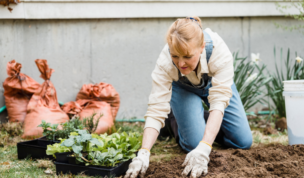 Women kneeling down moving dirt to plant a vegetable outside by her house.