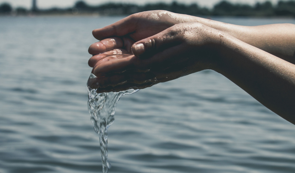 Hands holding water in their hand over a body of water