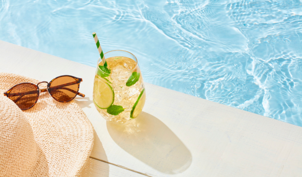 Sun hat and sunglasses next to a drink by the pool