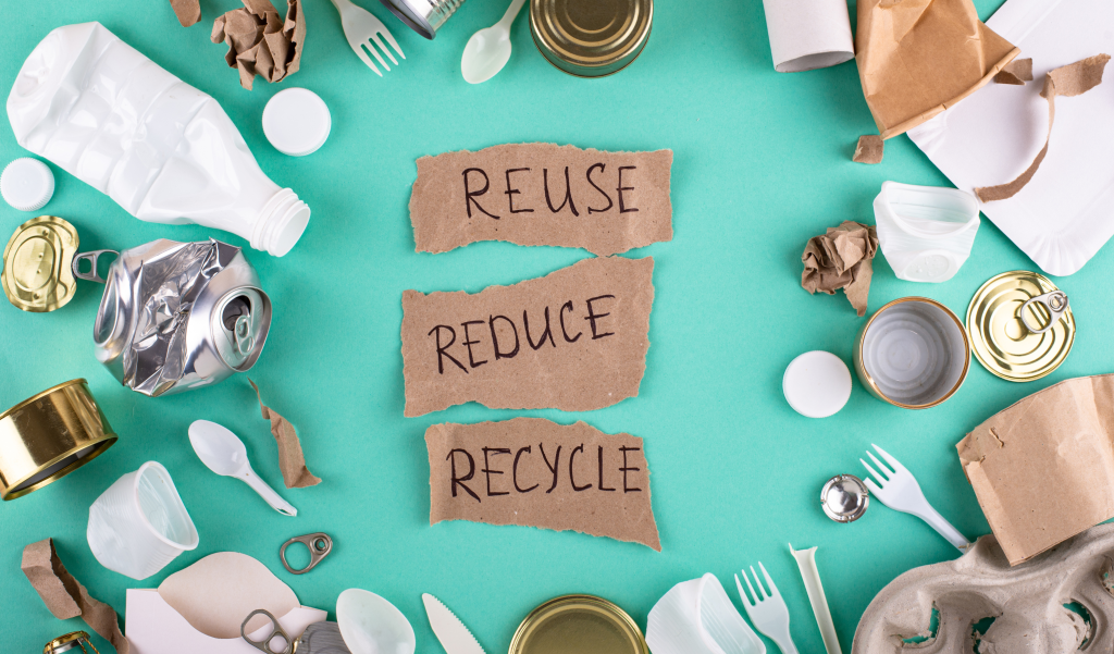 Reduce, reuse, recycle written on paper and surrounded by waste items.