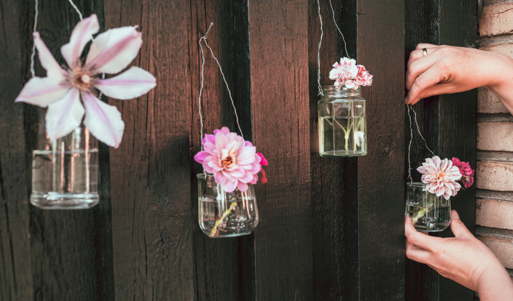 Person hanging flowers in upcycled glass jars.