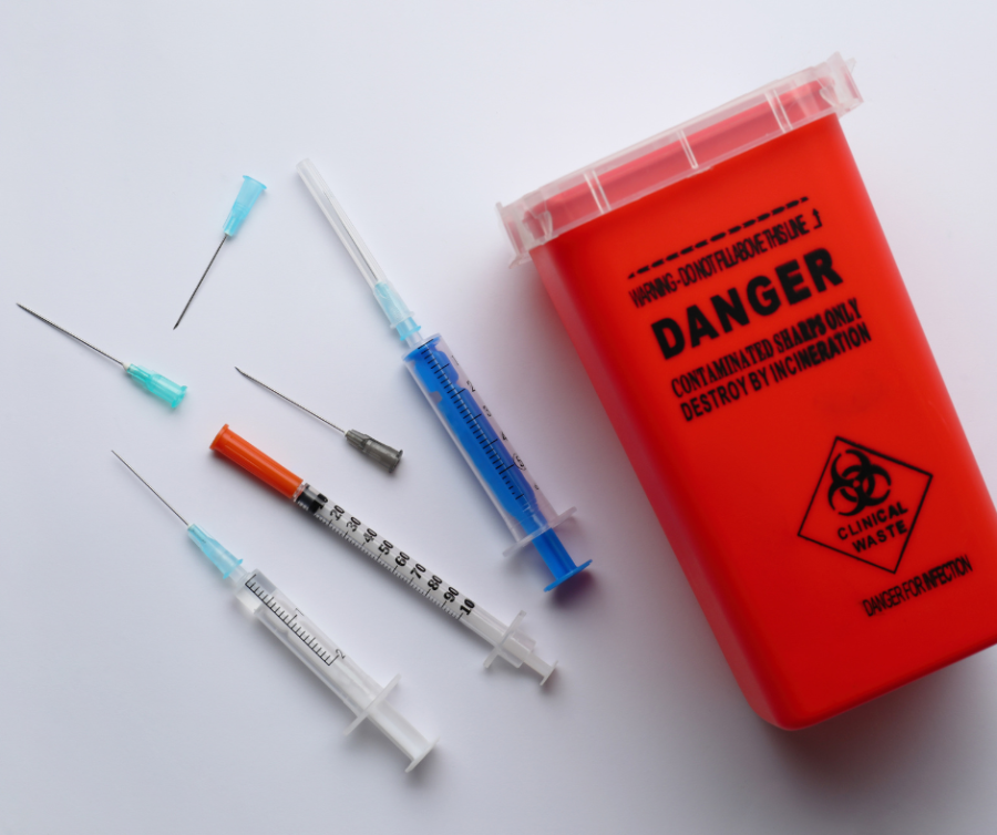 Sharps and syringes next to a sharps container.