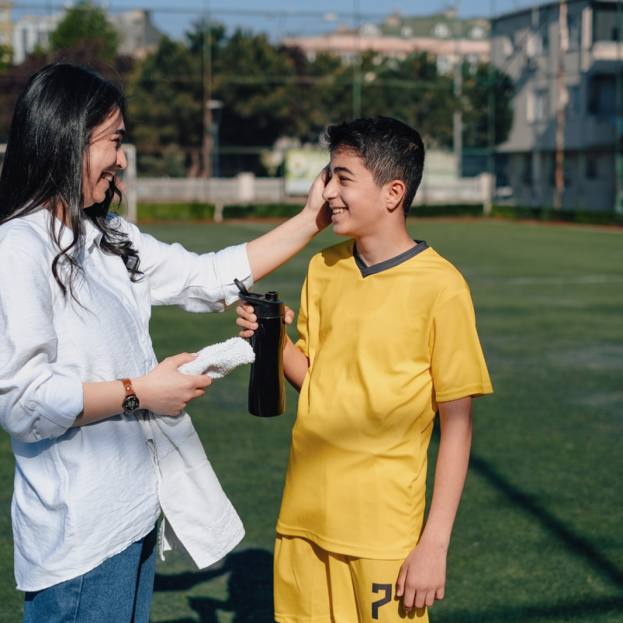 a boy takes a break on the field with a reusable water bottle and his mom 