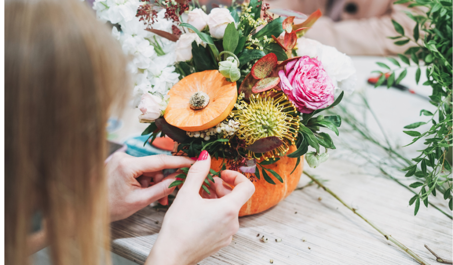 A woman putting flowers in a pumpkin vase.