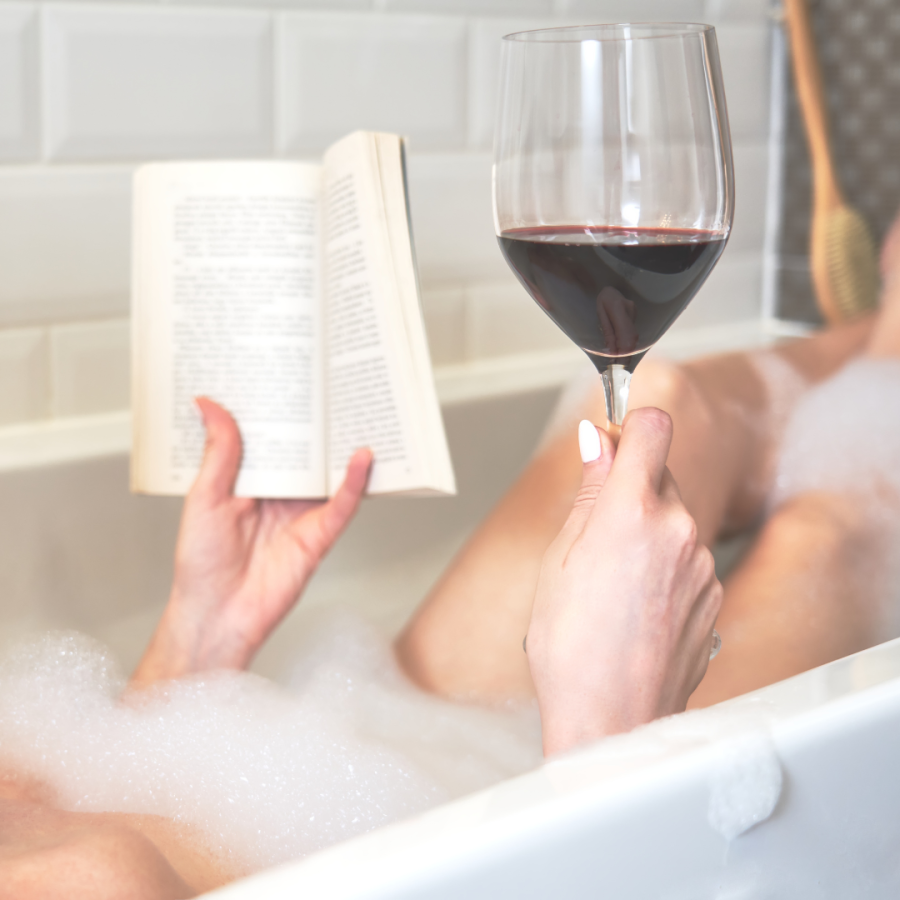 a woman soaks in a tub reading and drinking wine 