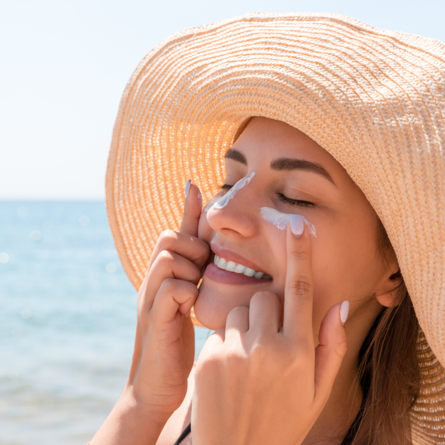 a woman applies sunscreen to her face on the beach 