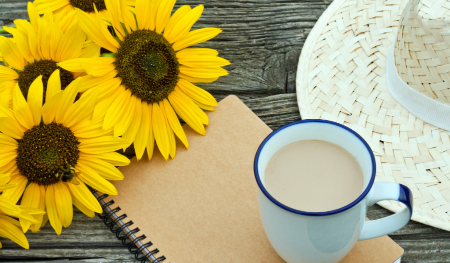 Coffee and a journal next to a sun hat and sunflowers
