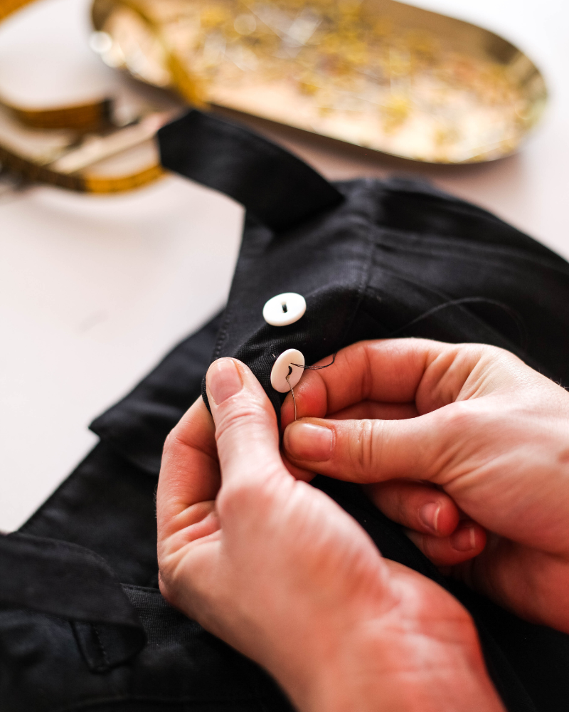 Person sewing a button on a black shirt.