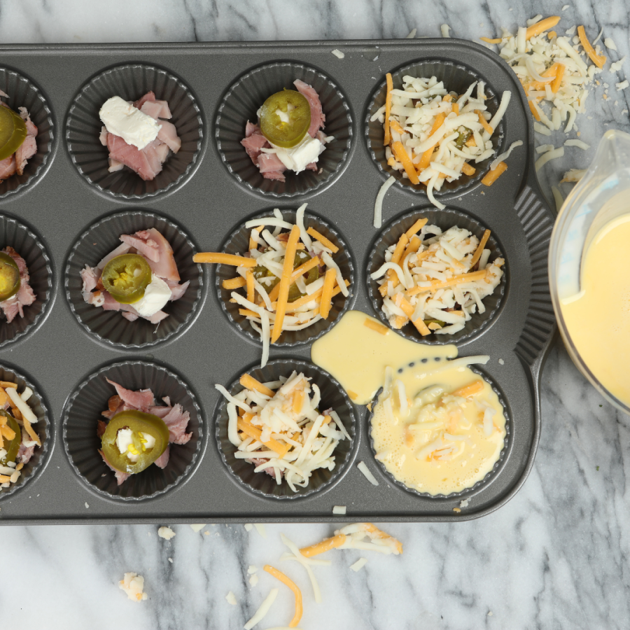 a muffin tin filled with egg and toppings ready for the oven 
