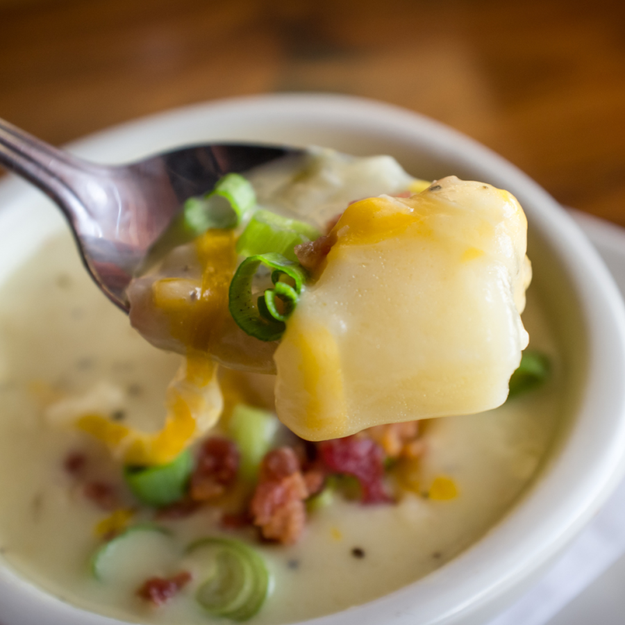 a hearty bowl of potato soup topped with cheese, bacon and chives 