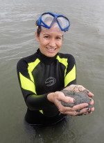 Sarah in a wetsuit, hip deep in water, holding a mud sample
