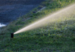 automatic sprinkler head spraying water over a green lawn