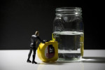 Action figure with tape measure measuring glass of water
