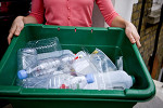 Person holding green bin full of plastic bottles