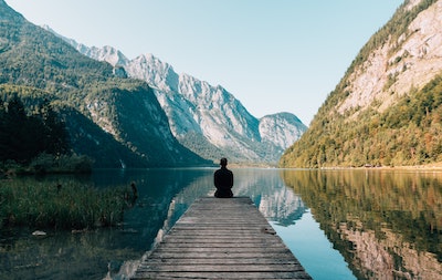 person sitting on pier overlooking lake among mountains